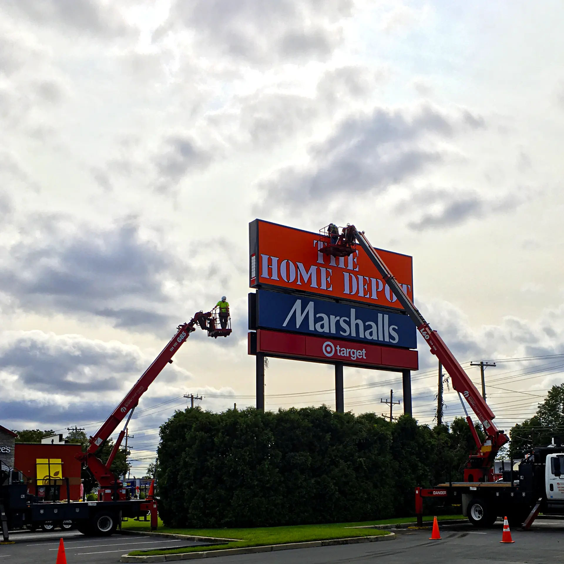 Two boom lifts servicing a multi-tenant pylon sign with The Home Depot, Marshalls, and Target panels
