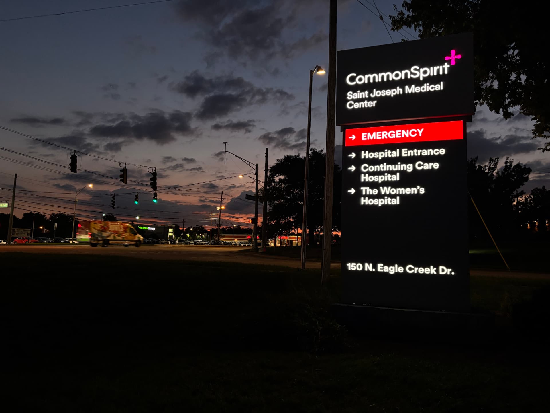 Illuminated CommonSpirit Saint Joseph Medical Center directory pylon glowing at dusk with red Emergency band