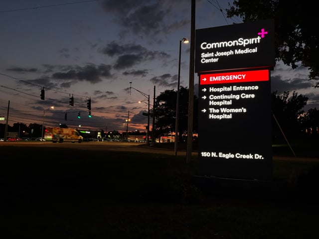 Illuminated CommonSpirit Saint Joseph Medical Center directory pylon glowing at dusk with red Emergency band