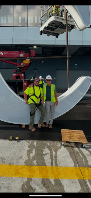 Jeff Petersen and Jeff Petersen Jr. standing beneath a large sign element during installation.