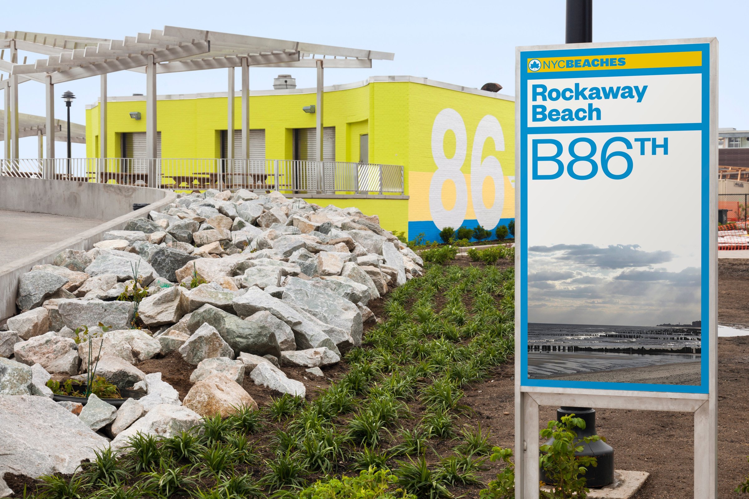 NYC Beaches Rockaway Beach B86th post-mounted identification sign beside a yellow beach building