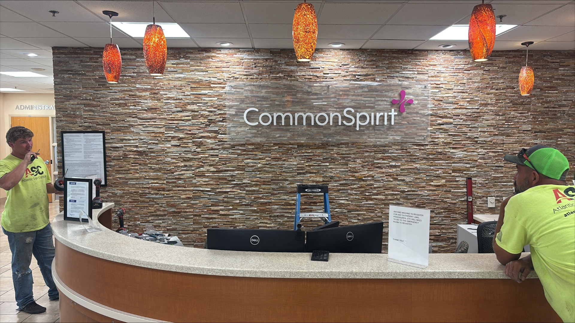AIS installers fitting a dimensional CommonSpirit logo on the stone reception wall of a hospital lobby