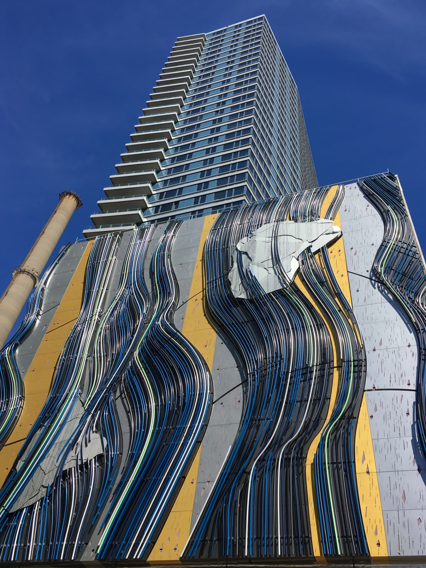 Large-scale architectural metal art installation with flowing polished and colored steel ribbons on a building facade