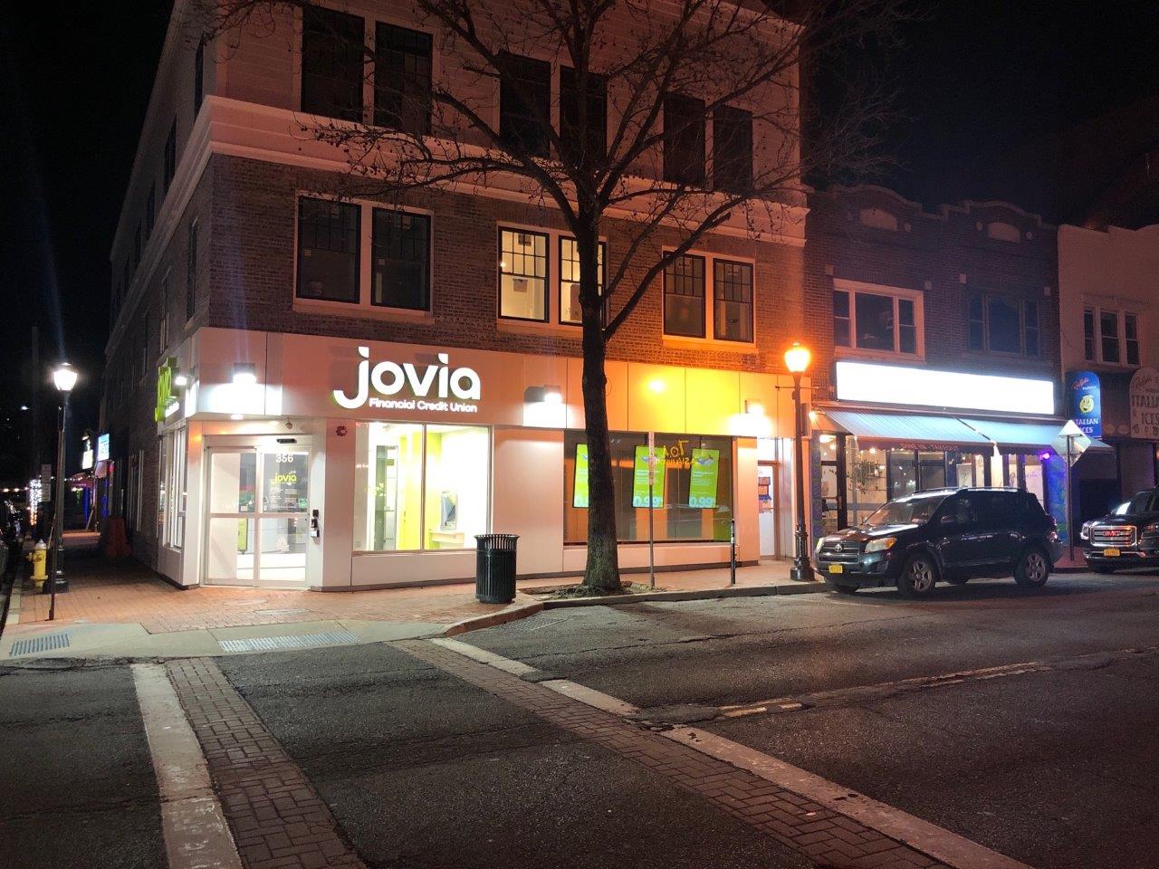 Jovia Financial Credit Union illuminated corner branch signage at night