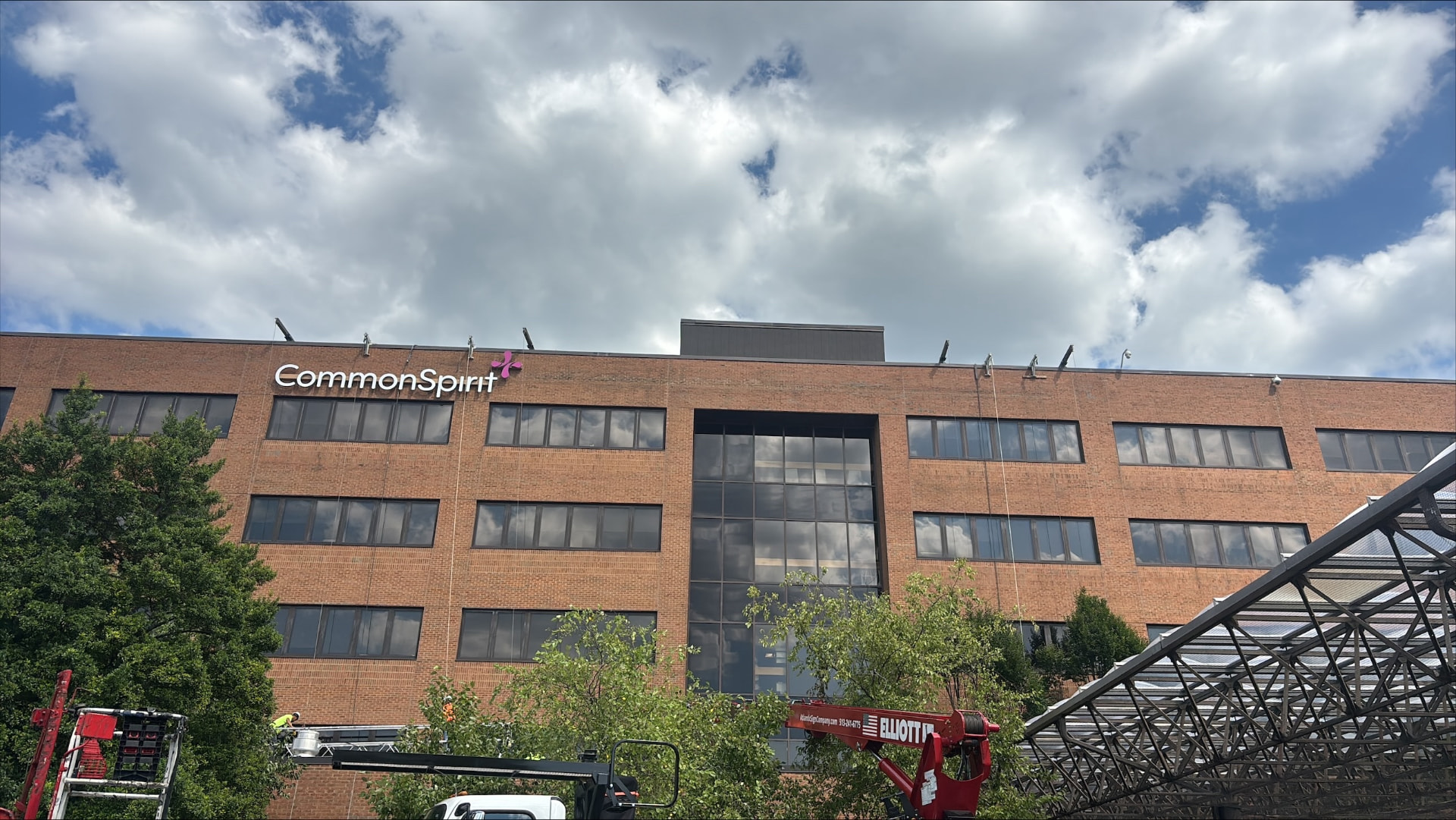 AIS lift crews installing illuminated CommonSpirit letters and logo along the top of a brick hospital building