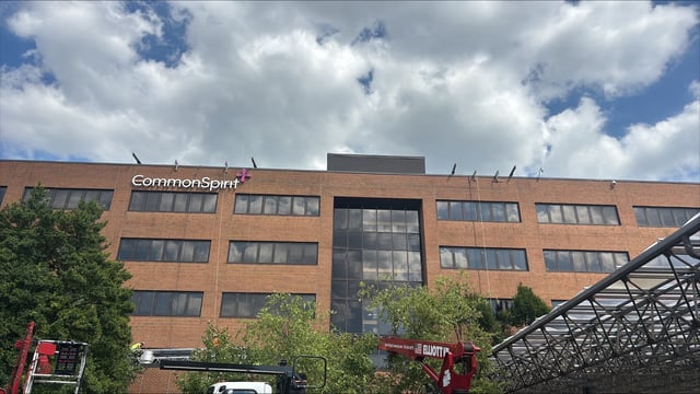 AIS lift crews installing illuminated CommonSpirit letters and logo along the top of a brick hospital building