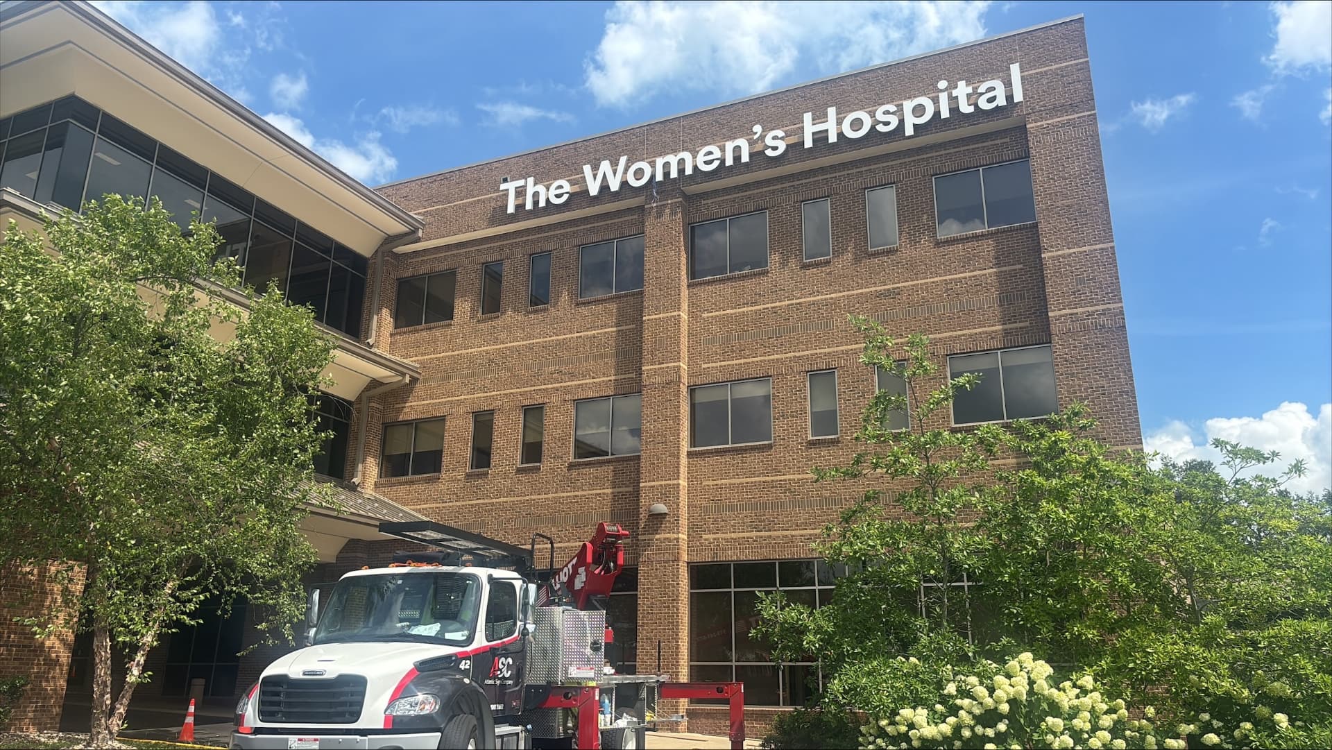 AIS crane truck installing The Women's Hospital white channel letters high on a brick facade
