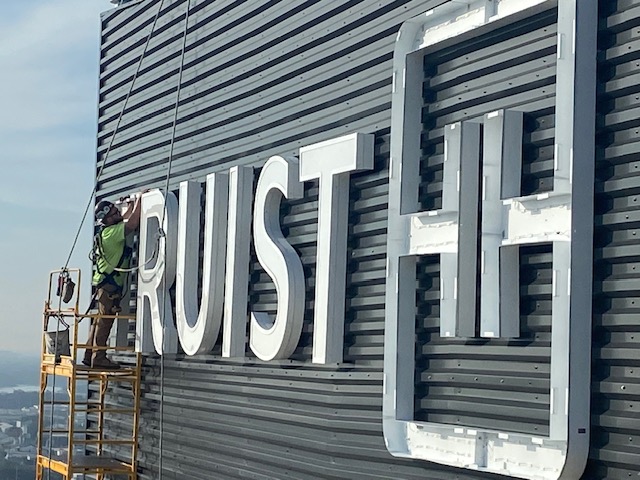 Installer setting dimensional Truist channel letters on a high-rise tower facade
