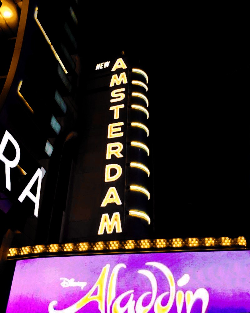 New Amsterdam Theatre vertical blade sign illuminated with exposed bulbs above an Aladdin marquee