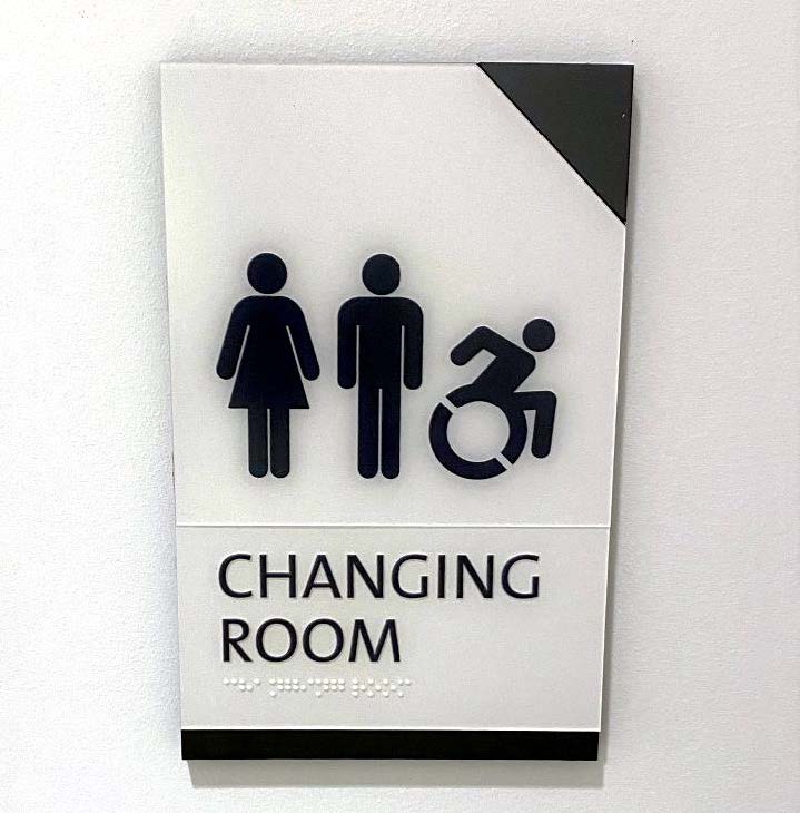 Wall-mounted ADA-compliant changing room sign with tactile icons, Braille, and modern finish