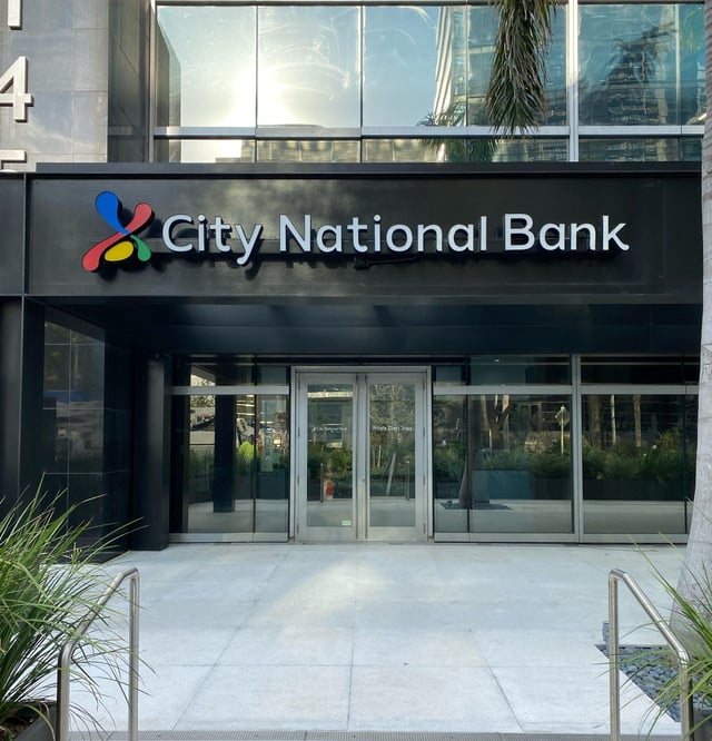 Illuminated bank entrance signage above a glass building entryway